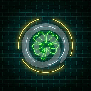 Neon glowing clover leaf sign in circle frames on a dark brick wall background. Green shamrock