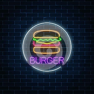 Neon glowing sign of burger in circle frame on a dark brick wall background. Fastfood light billboard symbol.