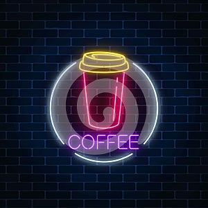 Neon glowing sign of coffee cup in circle frame on a dark brick wall background. Fastfood light billboard sign.