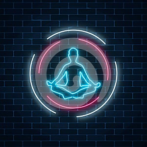 Neon glowing sign of yoga exercices club with lotus pose in circle frames on dark brick wall background.