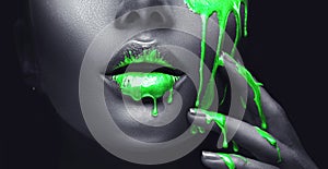 Neon green paint smudges drips from the face lips and hand, green liquid drops on beautiful model girl`s mouth