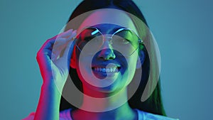 Neon light people. Positive asian lady model in eyeglasses posing in bright neon lights, smiling over blue background