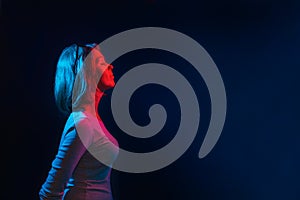 The neon lights of the club. Portrait of a young woman posing in profile. Blue and red light. Black background. Copy space