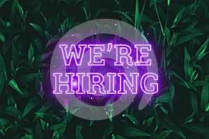 Neon pink inscription: We`re Hiring, on a green natural background. Concept for motivating background, business, self-development