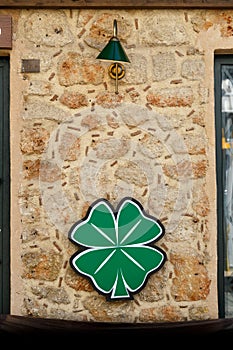 Neon sign 4-sheeted clover, on a stone wall under a green lamp.