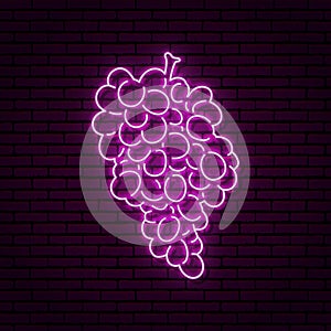 Neon sign in the form of a bunch of grapes. Against a brick wall with a shadow.