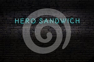 Neon sign. Word hero sandwich against brick wall. Night view