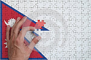 Nepal flag is depicted on a puzzle, which the man`s hand completes to fold