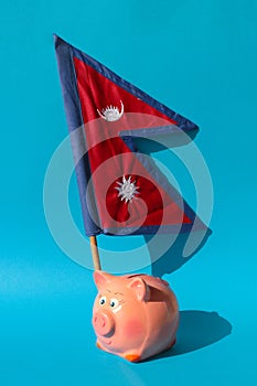 Nepalese flag and a piggy bank on a blue background. Savings or profitable investments in Nepal.