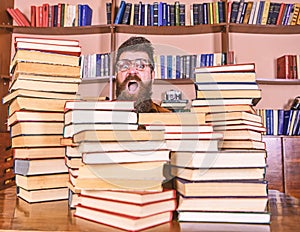 Nerd concept. Teacher or student with beard wears eyeglasses, sits at table with books, defocused. Man, nerd on