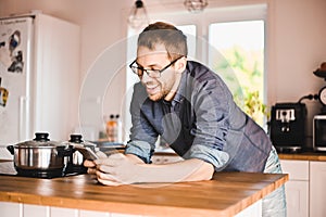 Nerd guy with glasses in stylish kitchen follows a recipe on the phone prepares chicken