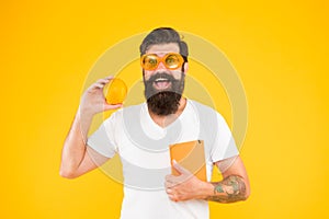 Nerd is the new cool. Bearded nerd man. Study nerd holding book and orange fruit on yellow background. Book nerd in