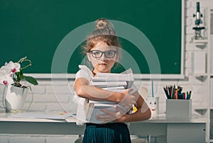 Nerd school girl in glasses with books on blackboard. Kid girl learning lesson at school. Elementary school child in