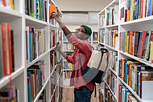 Nerd student african american man choosing book in university library taking it from shelf.