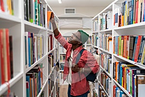 Nerd student african american man choosing book in university library taking it from shelf.