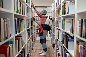 Nerd student african american man choosing book in university library taking it from shelf.