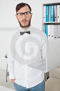 Nerdy businessman holding laptop looking at camera