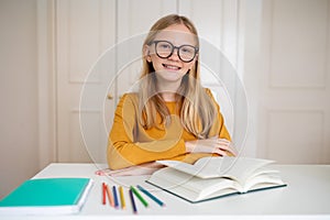 Nerdy teenage girl wearing glasses sitting at her desk with open book