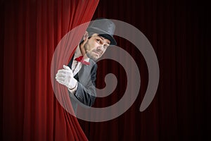 Nervous actor or illusionist is hiding behind red curtain in theater