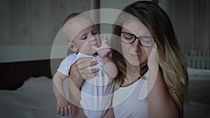 Nervous breakdown, tense young mother with headache holds infant on hands sitting on bed