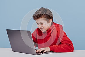 Nervous child boy in red sweatshirt typing on laptop