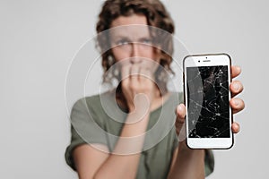 Nervous embarassed girl bites nails, holding her broken smartphone