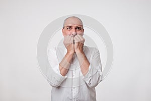 Nervous embarassed man bites nails. Mature businessman looks worried before visiting doctor or dentist.