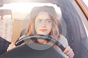 Nervous female driver sits at wheel, has worried expression as afraids to drive car by herself for first time. Frightened woman ha