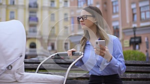 Nervous female manager working smartphone swinging baby carriage, multitasking