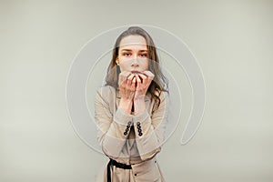 Nervous female worker in a suit bites her nails and looks into the camera with excitement, isolated on a beige background