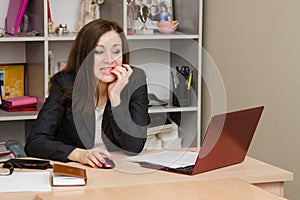 Nervous girl in office bites his nails, working on computer