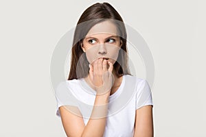 Nervous insecure young woman biting nails isolated on grey background