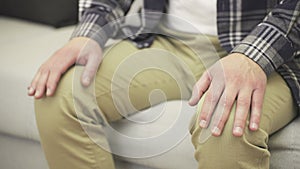 Nervous man sitting on sofa while holding hands on knees. Slow motion