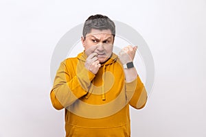 Nervous middle aged man biting finger nails and looking at his wrist clock with anxious.