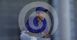 Nervous mixed race female baseball player, sitting on bench waiting, holding baseball bal