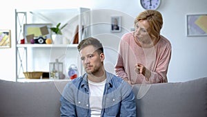 Nervous mother talking to adult son sitting on sofa at home, family conflict