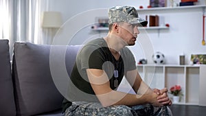Nervous soldier sitting on sofa at home, suffering PTSD, psychological problem