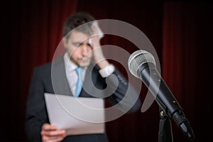 Nervous speaker is afraid of public speech and is sweating. Microphone in front.