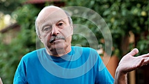 Nervous stressed mature man feeling awkward looking with doubt at camera standing on formal garden backgro