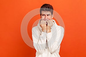 Nervous terrified teenager in white casual style sweatshirt biting his fingers with shocked look, fears and phobias