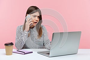 Nervous unhappy woman office worker talking phone with client sitting at workplace, manager making order on laptop, booking