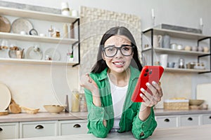 Nervous woman in glasses holding a red phone and looking forward to an important call or message