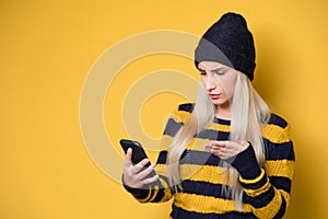 Nervous woman holding mobile phone, model wearing woolen cap and sweater, isolated on yellow background. No Wi-fi concept. Bad