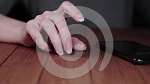 Nervous woman taps her fingers on the table and jerks the phone in anticipation of a call. Close-up of hands