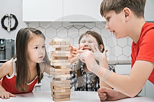 Nervous worried passionate kids playing board balance wooden brick tower game. Boy trying to move wooden cube out line