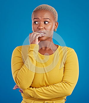 Nervous, worried and scared black woman in fear and bitting nails isolated against a studio blue background. Mental