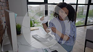 Nervous young African American woman tearing paper sitting at table in home office. Portrait of beautiful overburdened