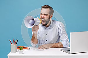 Nervous young bearded man in light shirt sit work at desk with pc laptop isolated on pastel blue background. Achievement