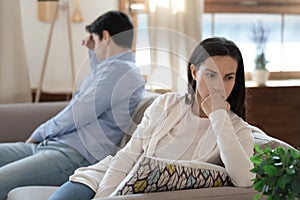 Nervous young couple sitting on sofa keeping silence after argument