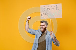 Nervous young protesting man hold protest sign broadsheet placard on stick clenching fist scream isolated on yellow